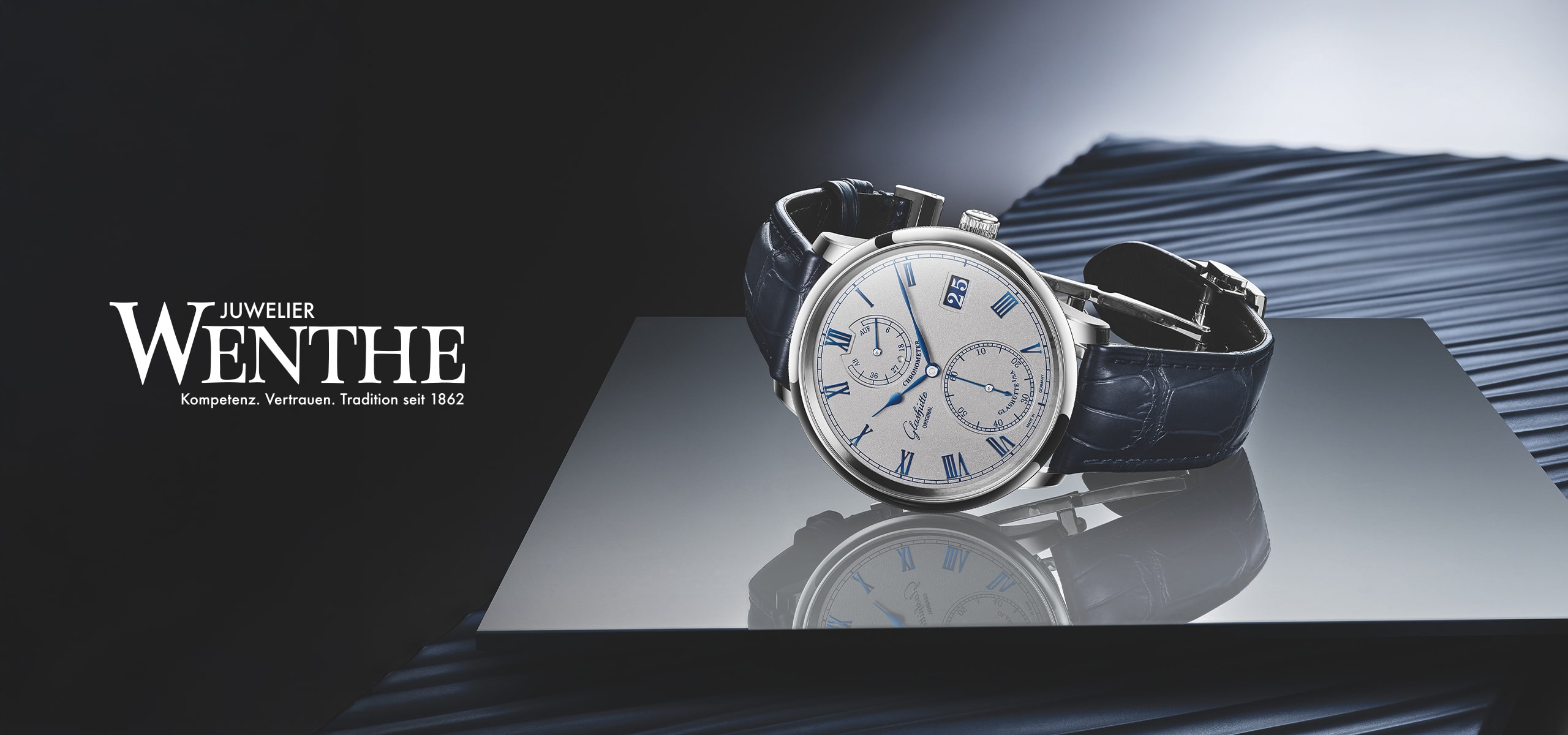 © Juwelier Wenthe Eine silberne Luxusarmbanduhr mit dunklem Lederarmband steht auf einer spiegelnden Fläche neben "Juwelier Wenthe", mit deutschem Schriftzug und einem stilvollen, dunklen Hintergrund, der die Highlights aus dem exklusiven Hauskatalog hervorhebt.