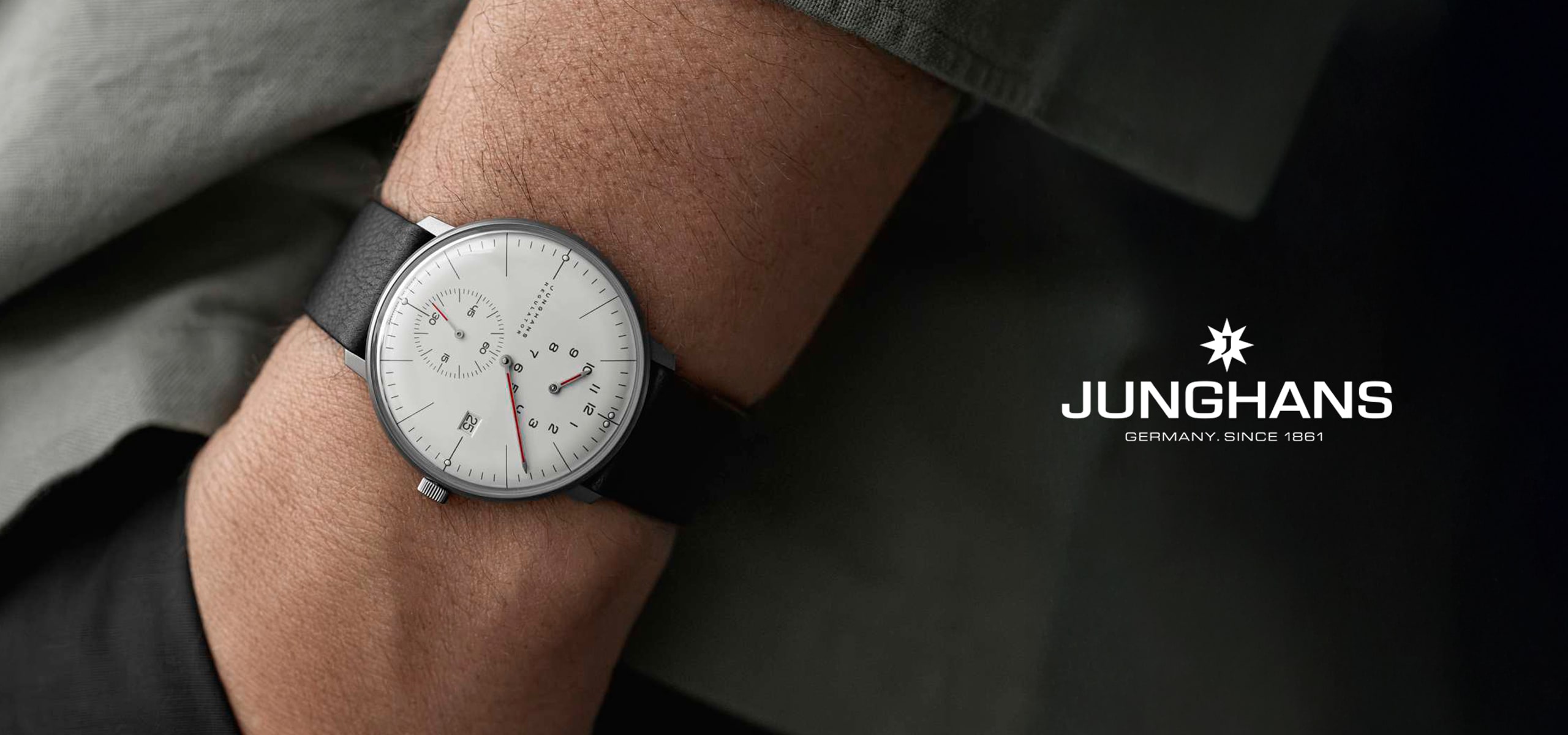 2025 © Junghans Eine Person trägt eine Junghans-Armbanduhr mit weißem Zifferblatt und schwarzem Lederarmband; auf dem minimalistischen Ziffernblatt ist rechts das Junghans-Logo und der Text "Germany. Seit 1861.".