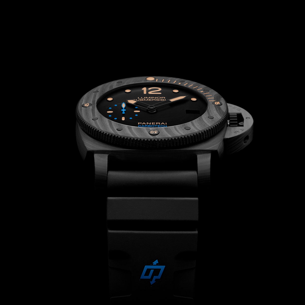 2025 © Panerai Eine Panerai Submersible Armbanduhr mit strukturierter Lünette, schwarzem Zifferblatt, goldenen Akzenten und blauen Details wird auf einem schwarzen Kautschukarmband mit blauem Panerai-Logo vor einem schlichten schwarzen Hintergrund präsentiert.
