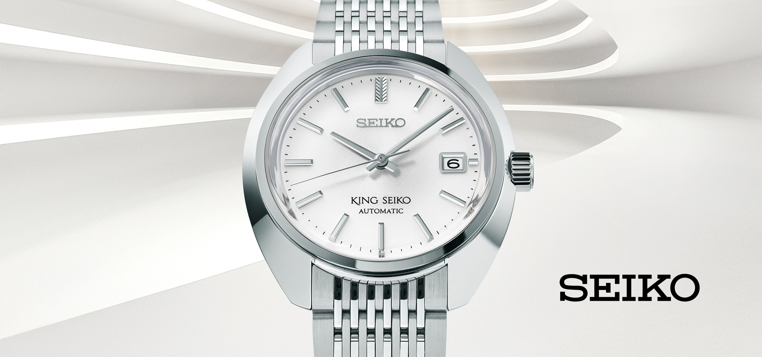 2025 © SEIKO Eine silberne Seiko King Seiko Automatik-Armbanduhr mit weißem Zifferblatt, Datumsanzeige und Metallarmband wird vor einem modernen weißen abstrakten Hintergrund präsentiert. Das SEIKO-Logo erscheint unten rechts und unterstreicht die kultige Handwerkskunst von Seiko.