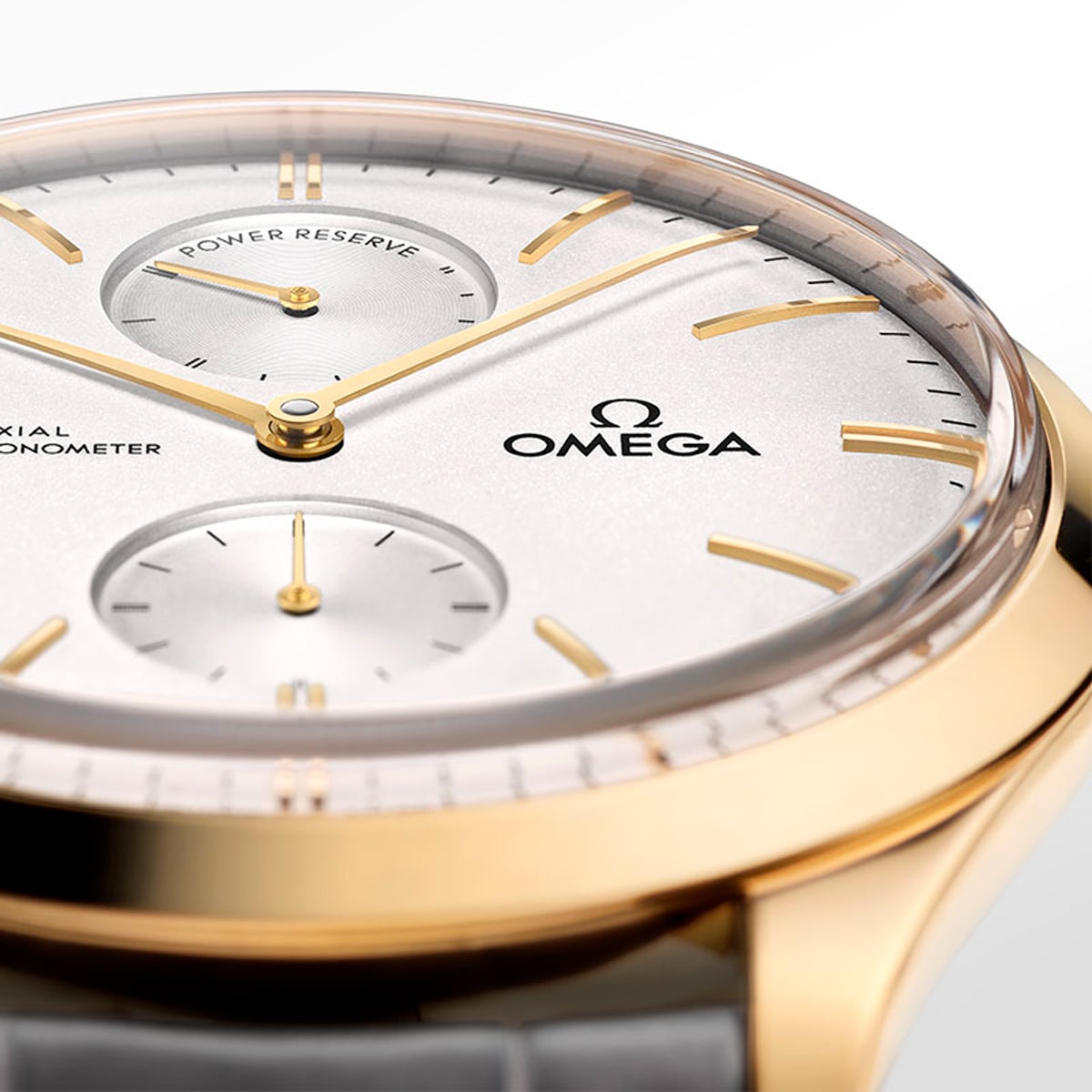 2025 © OMEGA Nahaufnahme einer Omega De Ville-Armbanduhr mit goldenem Gehäuse, weißem Zifferblatt und goldenen Indexen. Auf dem Zifferblatt sind zwei Hilfszifferblätter und das Omega-Logo zu sehen, gepaart mit einem eleganten grauen Lederarmband.