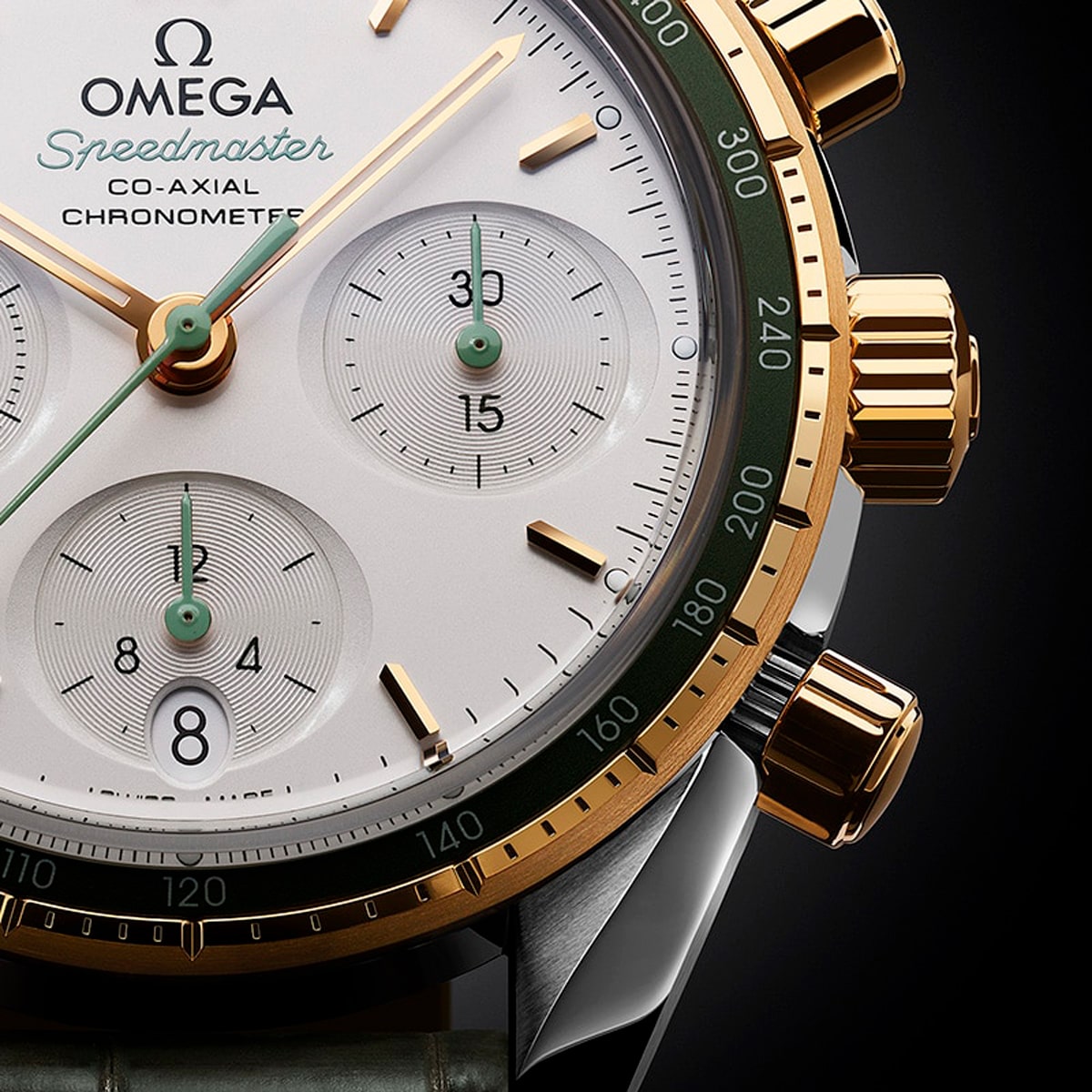 2025 © OMEGA Nahaufnahme einer Omega Speedmaster 38 mit weißem Zifferblatt, goldenen und grünen Akzenten, drei Hilfszifferblättern, goldenen Drückern und einer Lünette, die detaillierte Stunden-, Minuten- und Sekundenmarkierungen zeigt.