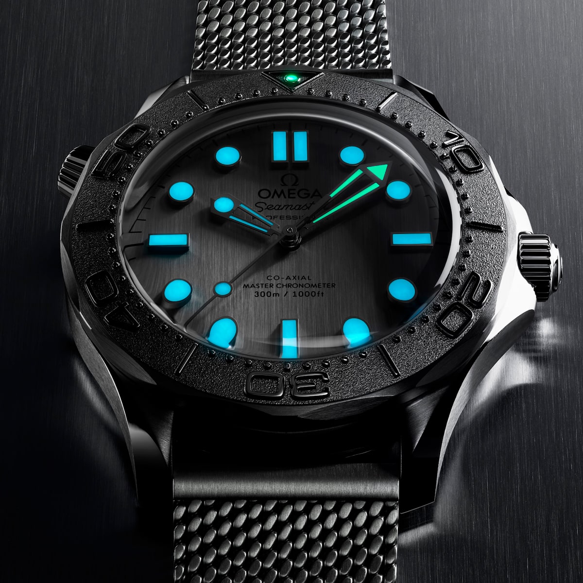 2025 © OMEGA Eine Nahaufnahme einer Omega Seamaster Diver 300M mit Metallarmband, schwarzer Lünette und blau leuchtenden Stundenmarkierungen und Zeigern, fotografiert vor einem dunklen, gebürsteten Metallhintergrund.