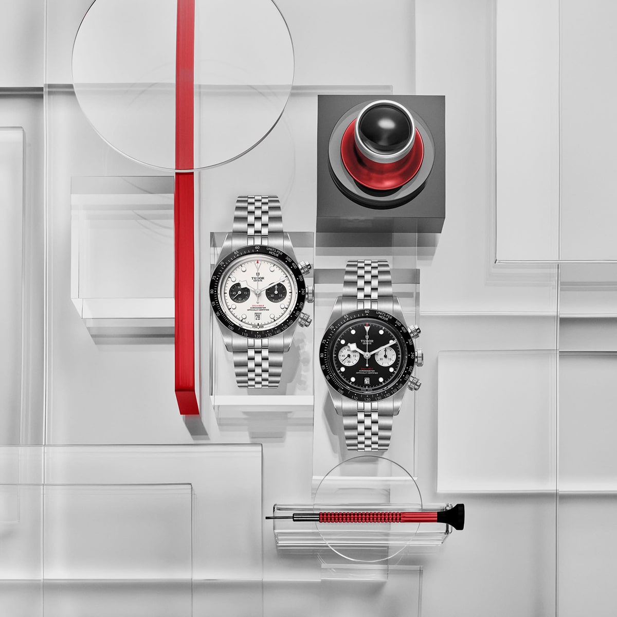 2025 © TUDOR Zwei Luxusarmbanduhren, darunter eine Black Bay Chrono mit Metallbändern, sind neben einem rot-schwarzen Knopf und einem Schraubenzieher mit rotem Griff auf einem geometrischen, durchscheinenden grau-weißen Hintergrund mit roten Akzenten zu sehen.