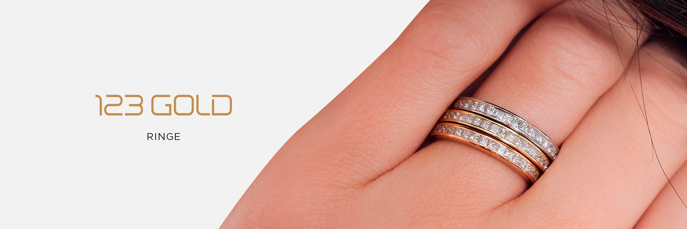 2025 © 123GOLD Nahaufnahme einer Hand, die drei übereinander liegende Gold- und Silberdiamantringe trägt; der Hintergrund ist weiß, und auf der linken Seite steht "123GOLD Ringe".