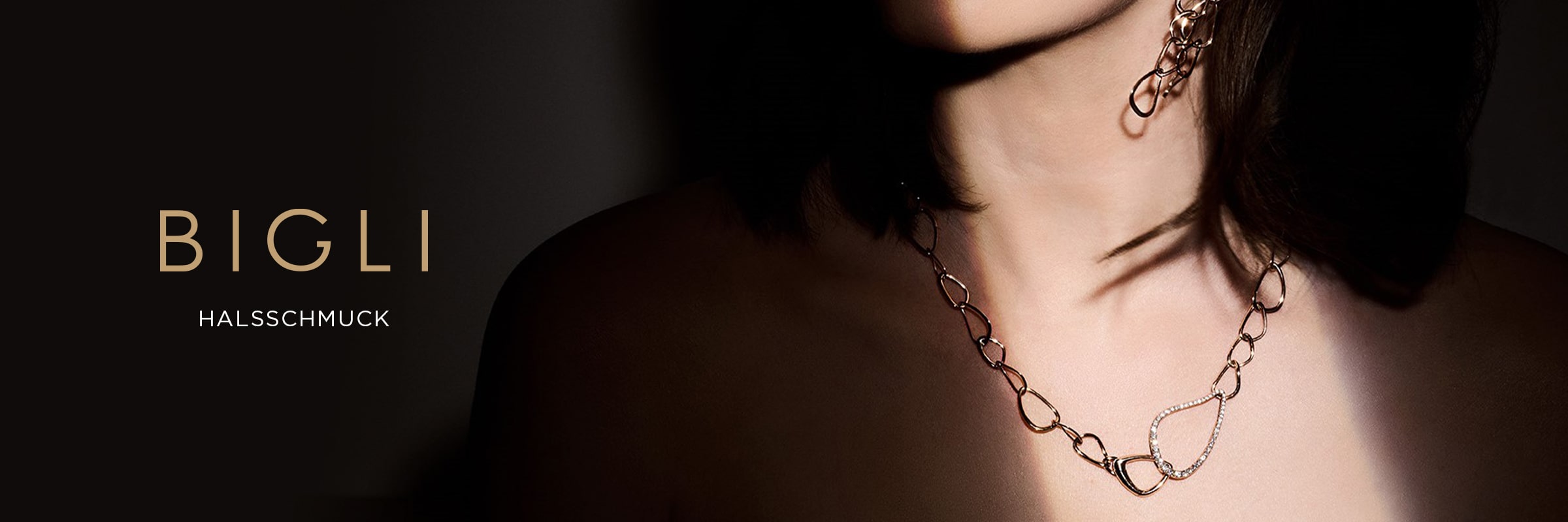 2025 © BIGLI Eine Frau trägt eine zarte BIGLI Halsschmuck-Kette und passende Ohrringe. Die linke Seite ihres Gesichts liegt im Schatten. Links daneben steht auf dunklem Hintergrund der Text "BIGLI HALSSCHMUCK".