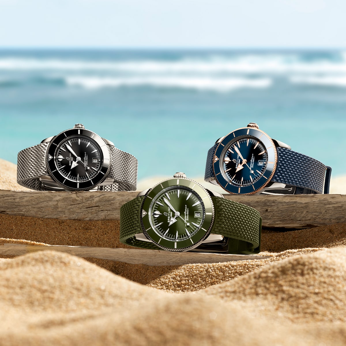 2025 © BREITLING Drei Breitling-Armbanduhren mit schwarzen, blauen und grünen Ziffernblättern sind auf Treibholz am Strand ausgestellt, wobei das Meer und der Himmel im Hintergrund verschwimmen.