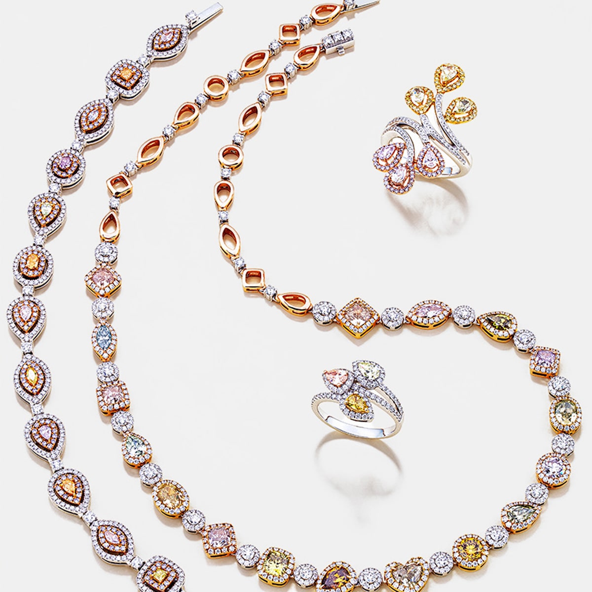 2025 © Diamond Group Ein elegantes Schmuckset von DiamondGroup mit Halsschmuck - zwei Halsketten und zwei Ringe mit mehrfarbigen Edelsteinen und Diamanten in komplizierten Gold- und Silberfassungen, wunderschön präsentiert auf weißem Hintergrund.
