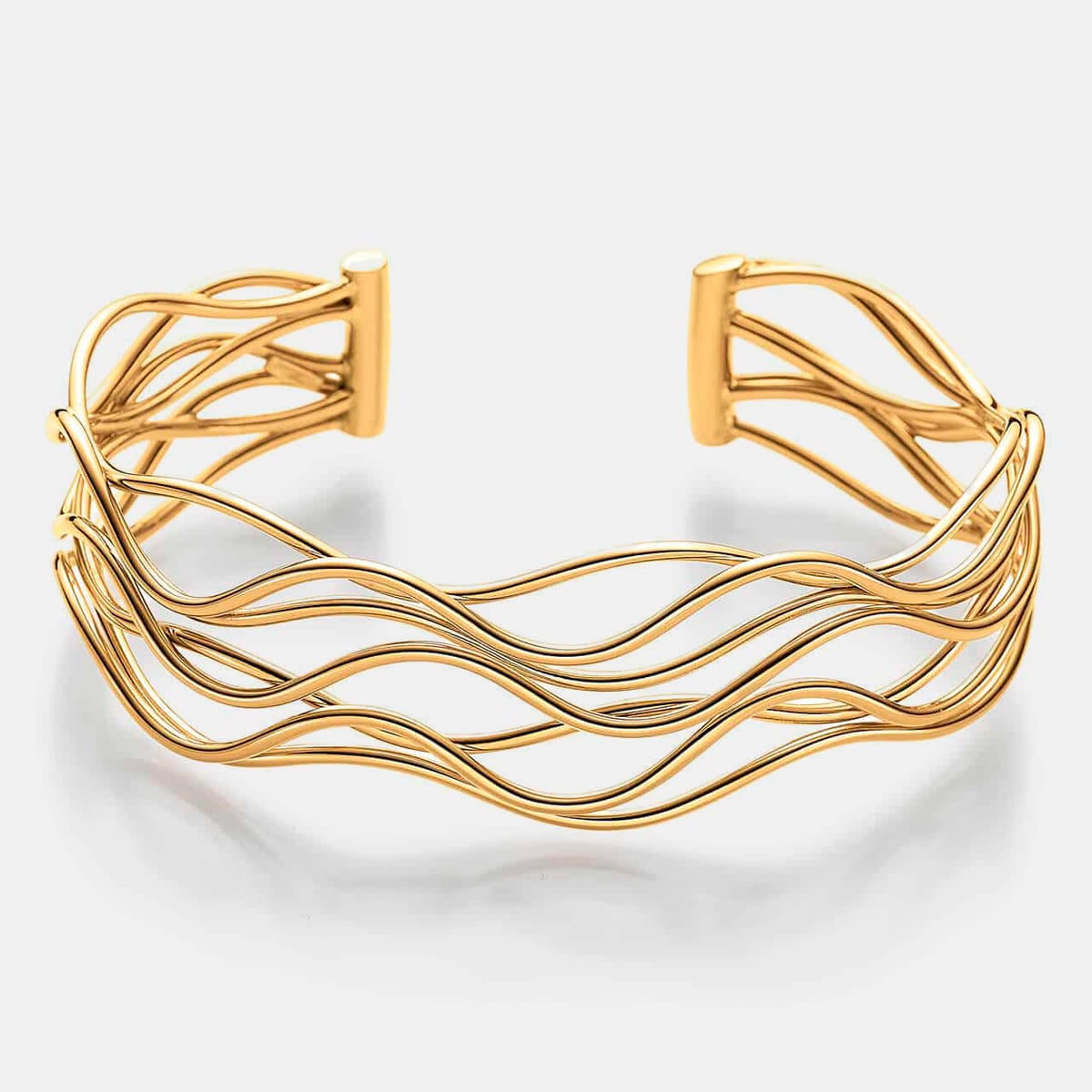 2025 © Elaine Firenze Ein goldenes Manschettenarmband von Elaine Firenze Armschmuck mit mehreren ineinander verwobenen, gewellten Bändern schafft ein fließendes, offenes Design vor einem schlichten weißen Hintergrund.