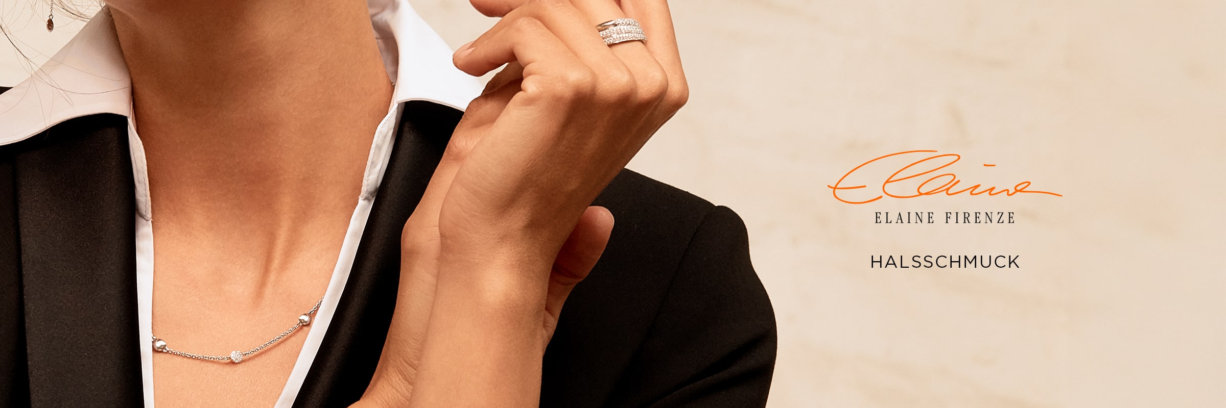 2025 © Elaine Firenze Eine Person in schwarzem Blazer und weißem Hemd trägt eine zarte silberne Elaine Firenze Halsschmuck-Halskette und mehrere Ringe, wobei eine Hand ihr Kinn berührt. Der Text lautet "Elaine Firenze HALSSCHMUCK" in Orange und Schwarz.