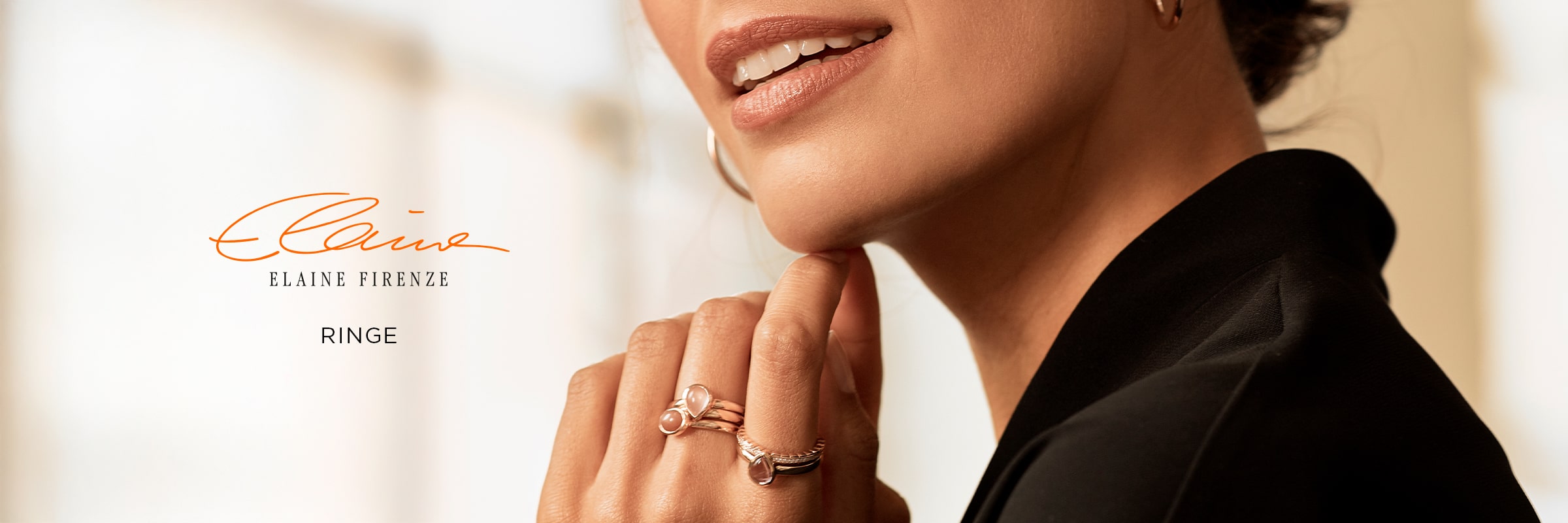 2025 © Elaine Firenze Eine Frau, die mehrere elegante Elaine Firenze Ringe trägt, berührt sanft ihr Kinn und stellt den exquisiten Schmuck zur Schau. Der Hintergrund ist sanft verschwommen, und der Text lautet "Elaine Firenze" und "Ringe".