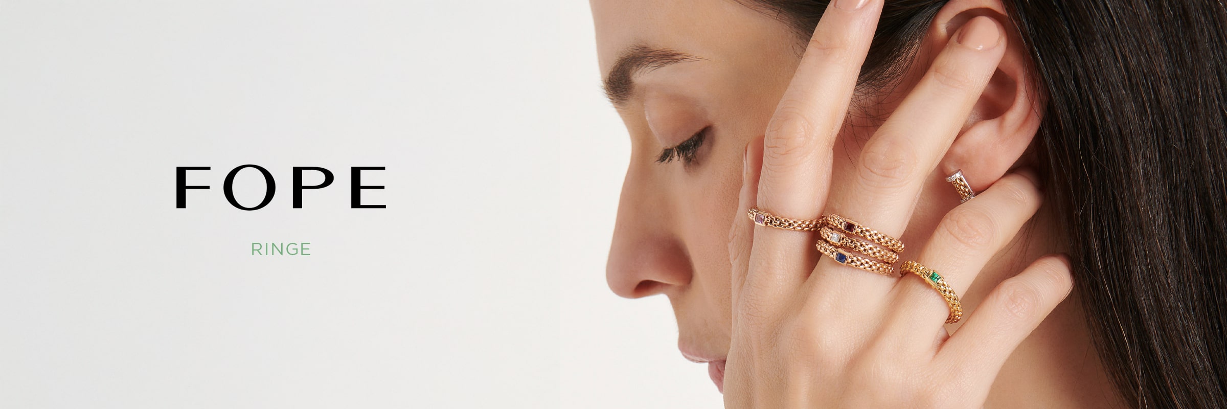 2025 © FOPE Eine Frau mit langen dunklen Haaren berührt ihr Gesicht und trägt elegant mehrere Goldringe von FOPE Ringe an ihren Fingern. Der Text auf der linken Seite lautet "FOPE RINGE" vor einem hellen Hintergrund.