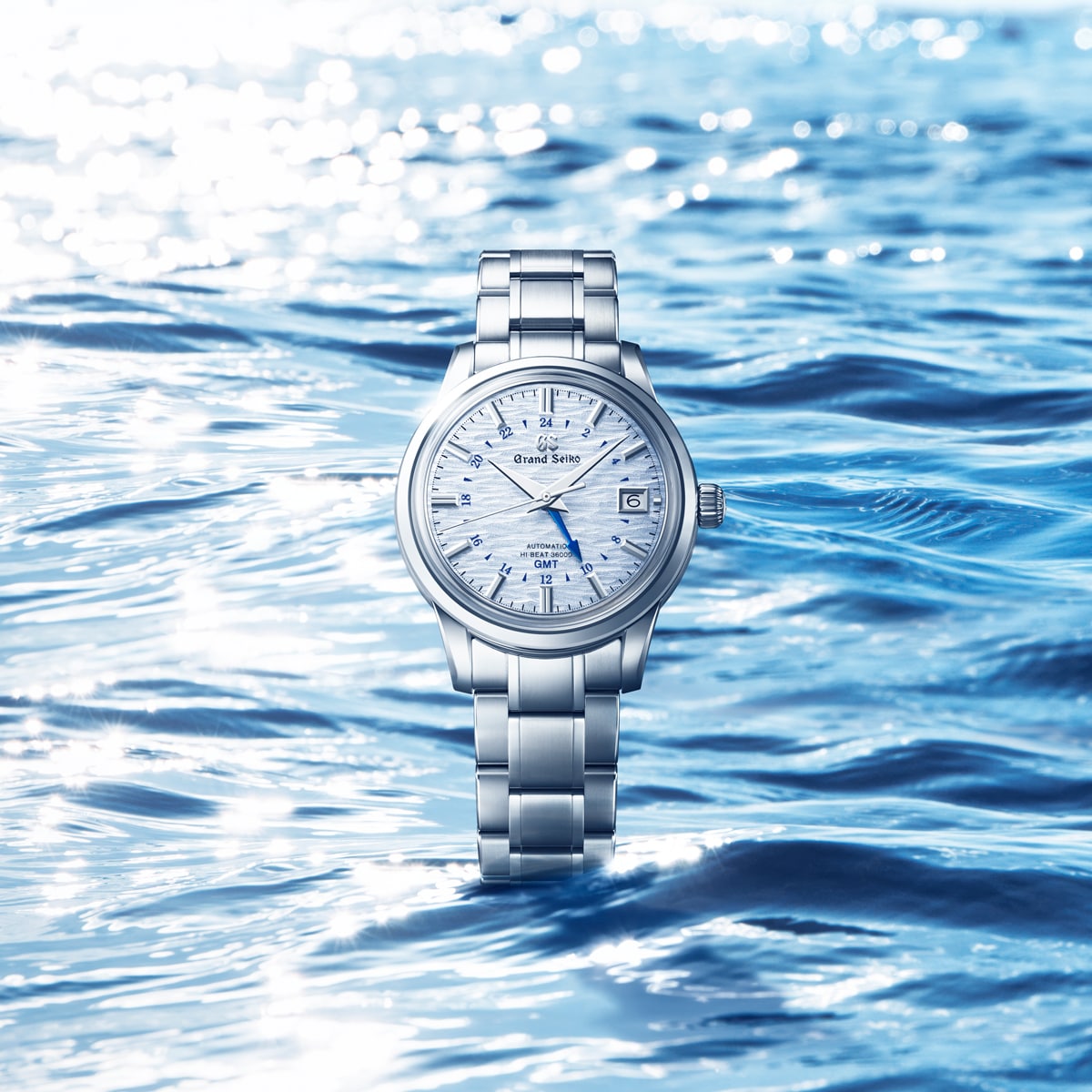 2025 © GRAND SEIKO Eine Grand Seiko Elegance Armbanduhr aus Edelstahl mit strukturiertem weißem Zifferblatt wird vor einem blau schimmernden Wasserhintergrund präsentiert, der exquisite Reflexe und Wellen einfängt.