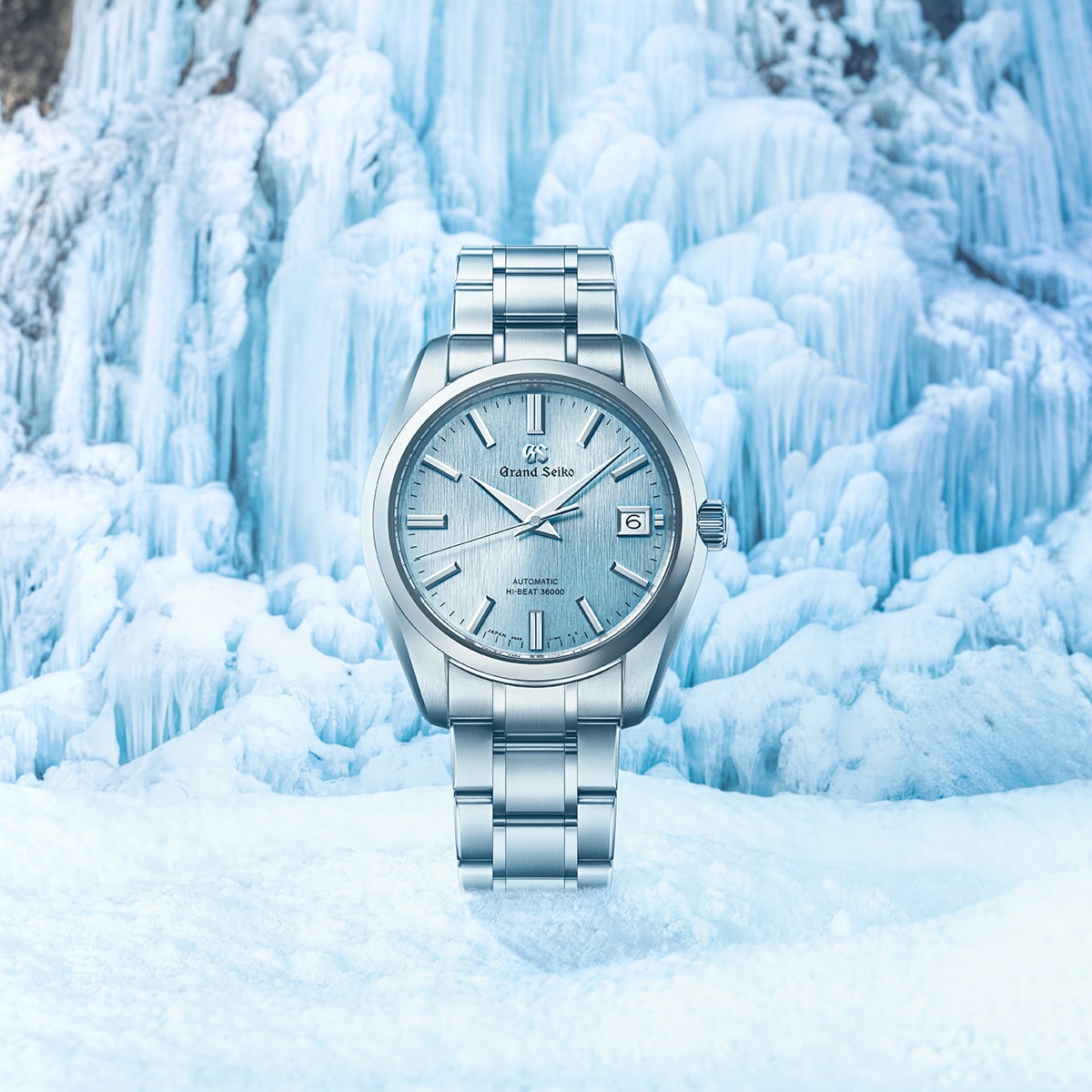 2025 © GRAND SEIKO Eine silberne Grand Seiko Heritage Armbanduhr mit eisblauem, strukturiertem Zifferblatt und Datumsanzeige vor einem Hintergrund aus eisigen, gefrorenen Formationen.