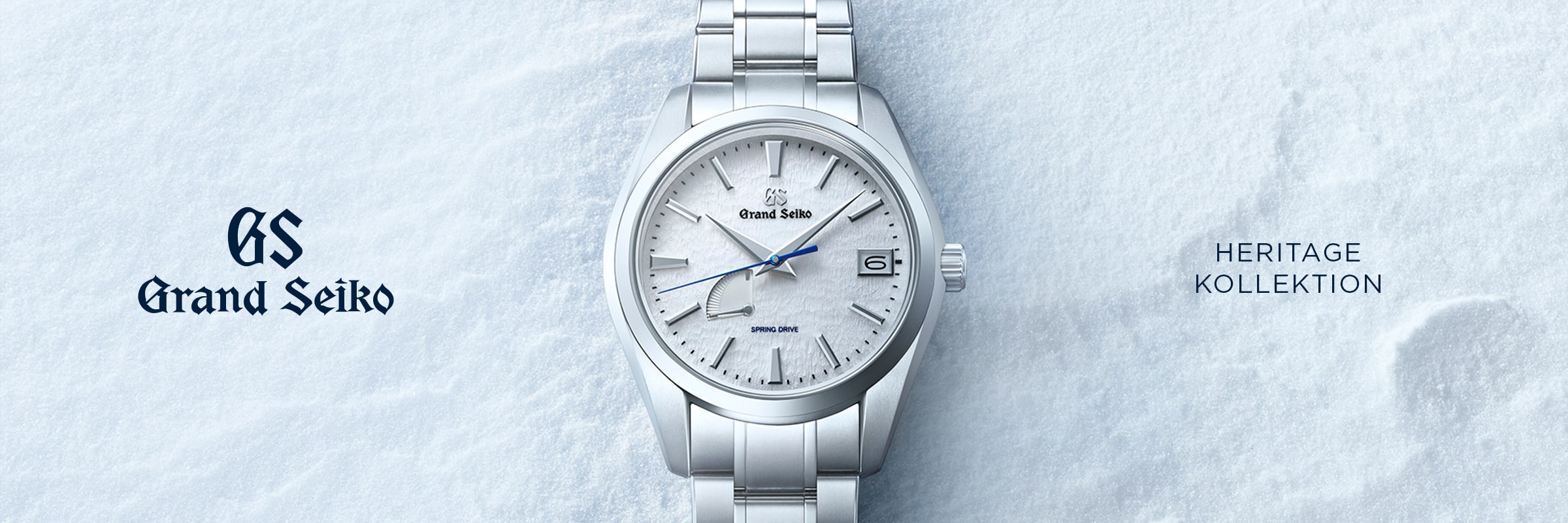 2025 © GRAND SEIKO Eine silberne Grand Seiko Heritage Armbanduhr mit strukturiertem weißem Zifferblatt ruht auf einer verschneiten Oberfläche. Das Grand Seiko Logo und der Schriftzug "HERITAGE KOLLEKTION" erscheinen links bzw. rechts neben der Uhr.