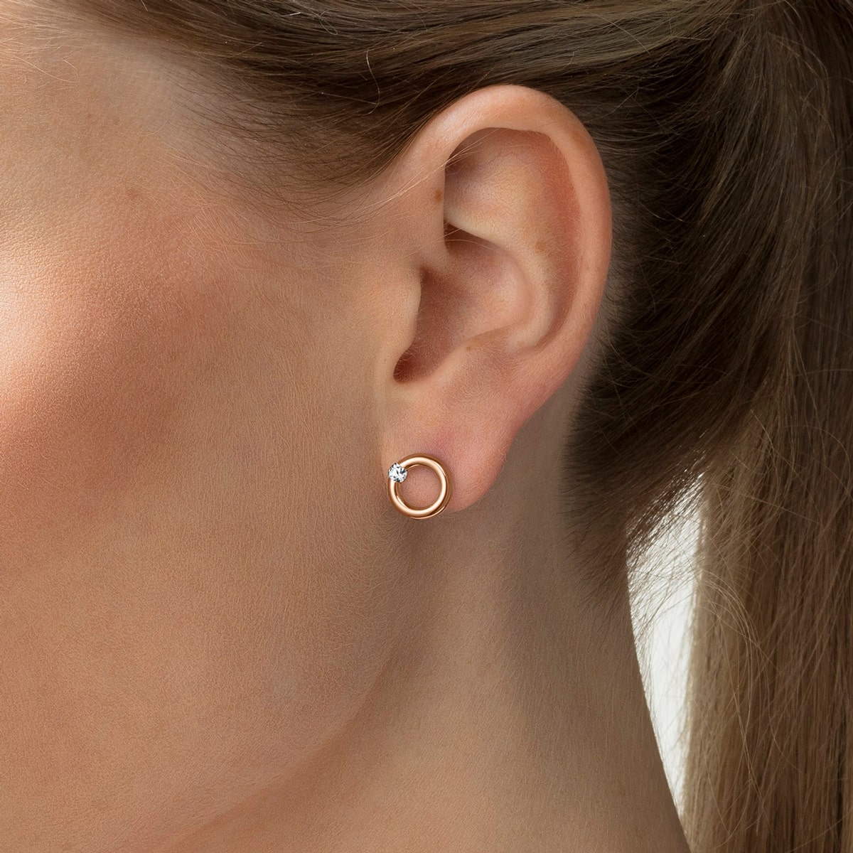 2025 © Niessing Nahaufnahme eines Frauenohrs mit Niessing Ohrschmuck: ein kleiner, kreisförmiger Ohrstecker aus Gold mit einem einzelnen klaren Edelstein als Akzent an der Spitze. Ihre helle Haut und ihr zurückgebundenes Haar unterstreichen das elegante Design.