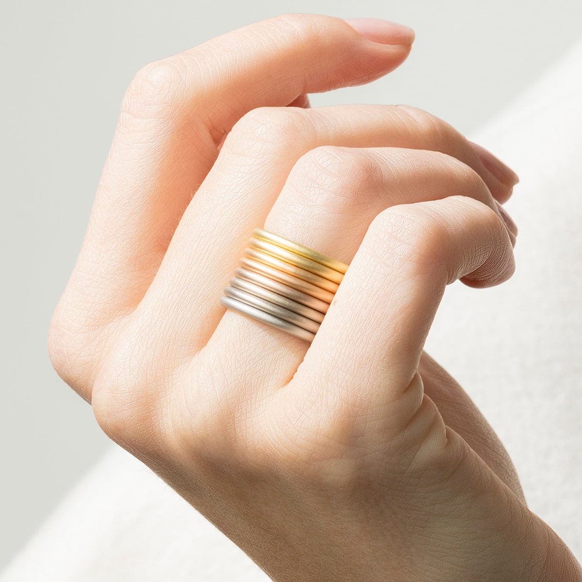 2025 © Niessing Eine Hand mit ordentlich manikürten Nägeln trägt am Mittelfinger einen Stapel von sechs glatten, minimalistischen Niessing Ringen in Gold- und Silbertönen, die sich vor einem weichen, hellen Hintergrund abheben.