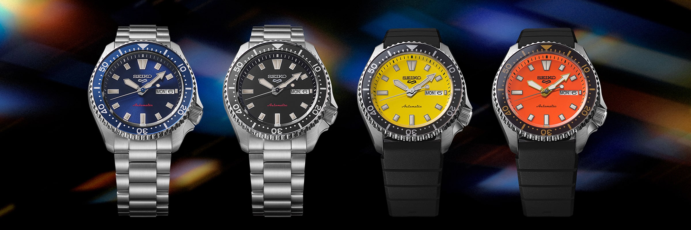 2025 © SEIKO Vier Seiko 5 Sports Taucheruhren in einer Reihe: blaues Zifferblatt mit silbernem Band, schwarzes Zifferblatt mit silbernem Band, gelbes Zifferblatt mit schwarzem Band und oranges Zifferblatt mit schwarzem Band - alle vor einem dunklen, abstrakten Hintergrund.