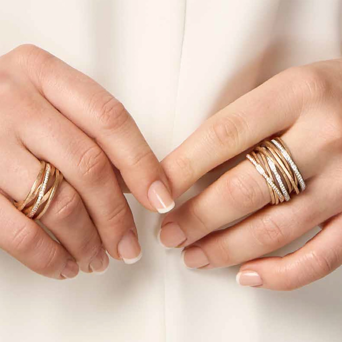2025 © Schmuckwerk Eine Person mit ordentlich manikürten Nägeln trägt mehrere Lagen Schmuckwerk Ringe in Gold und Silber, die jeweils ein gedrehtes und strukturiertes Muster aufweisen, zu einem hellen Outfit.