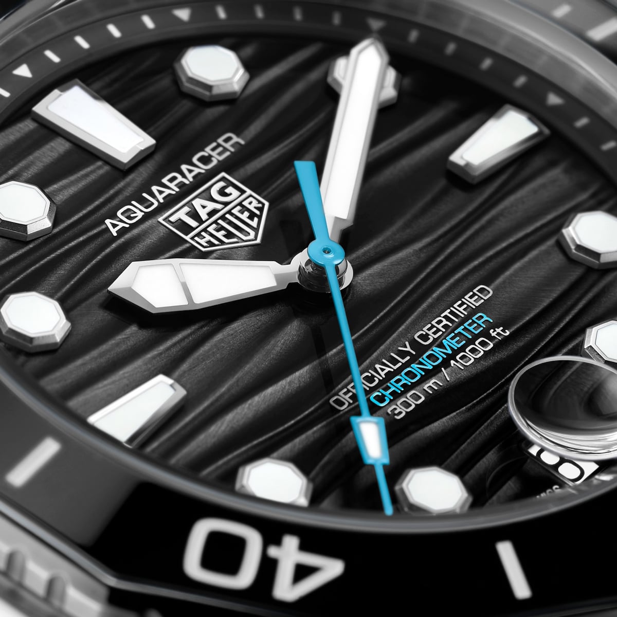2025 © TAG HEUER Nahaufnahme des Ziffernblatts einer TAG Heuer Aquaracer mit fetten weißen Stundenmarkierungen, einem blauen Sekundenzeiger und dem Hinweis, dass es sich um einen offiziell zertifizierten Chronometer handelt, der bis 300 Meter (1000 Fuß) wasserdicht ist.