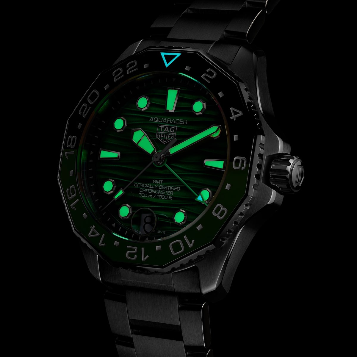 2025 © TAG HEUER Eine schwarze TAG Heuer Aquaracer-Armbanduhr mit grün leuchtenden Zeigern, Markierungen und Details in dunkler Umgebung unterstreicht die für die TAG Heuer Aquaracer charakteristischen lumineszierenden Merkmale für maximale Sichtbarkeit.