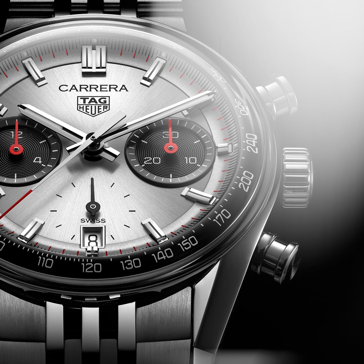 2025 © TAG HEUER Nahaufnahme einer TAG Heuer Carrera Chronographenuhr mit silbernem Zifferblatt, schwarzen und roten Hilfszifferblättern und einem Datumsfenster bei 6 Uhr. Das Gehäuse und das Armband aus Edelstahl schimmern, wenn das Licht auf die rechte Seite fällt.