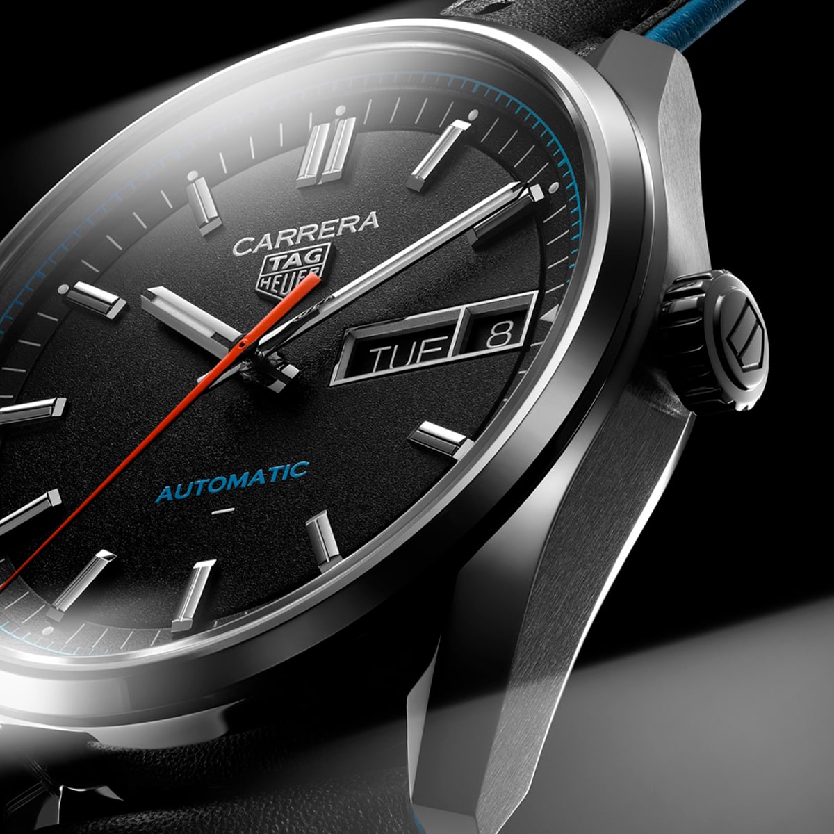 2025 © TAG HEUER Nahaufnahme einer TAG Heuer Carrera Automatik-Armbanduhr mit schwarzem Zifferblatt, silbernen Stundenmarkierungen, Tages- und Datumsanzeige, rotem Sekundenzeiger und "AUTOMATIC" in blauer Schrift. Die TAG Heuer Carrera verfügt über ein elegantes schwarzes Lederarmband.