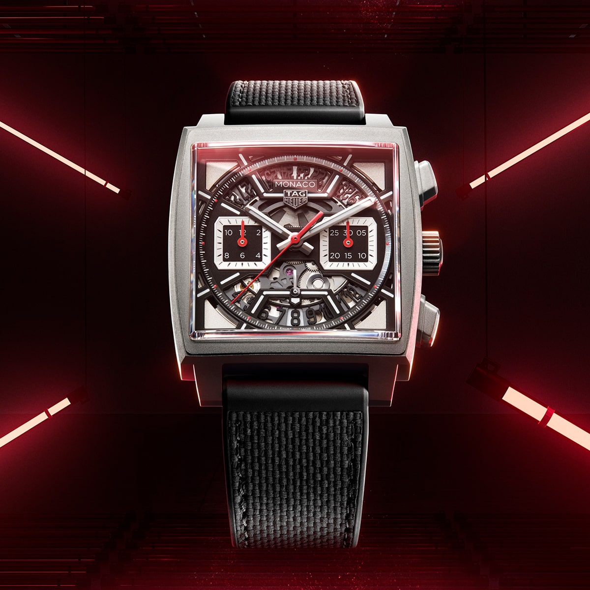2025 © TAG HEUER Eine quadratische TAG Heuer Monaco-Armbanduhr mit skelettiertem Zifferblatt und schwarzem Armband vor einem dunklen Hintergrund, der von roten Neonlichtern und auffälligen geometrischen Reflexen beleuchtet wird.