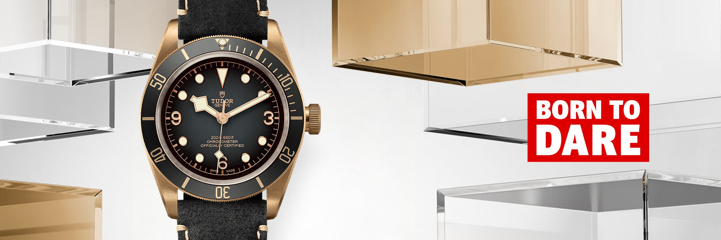 2025 © TUDOR Eine Black Bay Bronze Tudor-Armbanduhr mit schwarzem Armband ist vor einem Hintergrund aus schwebenden Gold- und Klarglasblöcken ausgestellt. Rechts daneben steht in einem rot-weißen Kasten "BORN TO DARE".