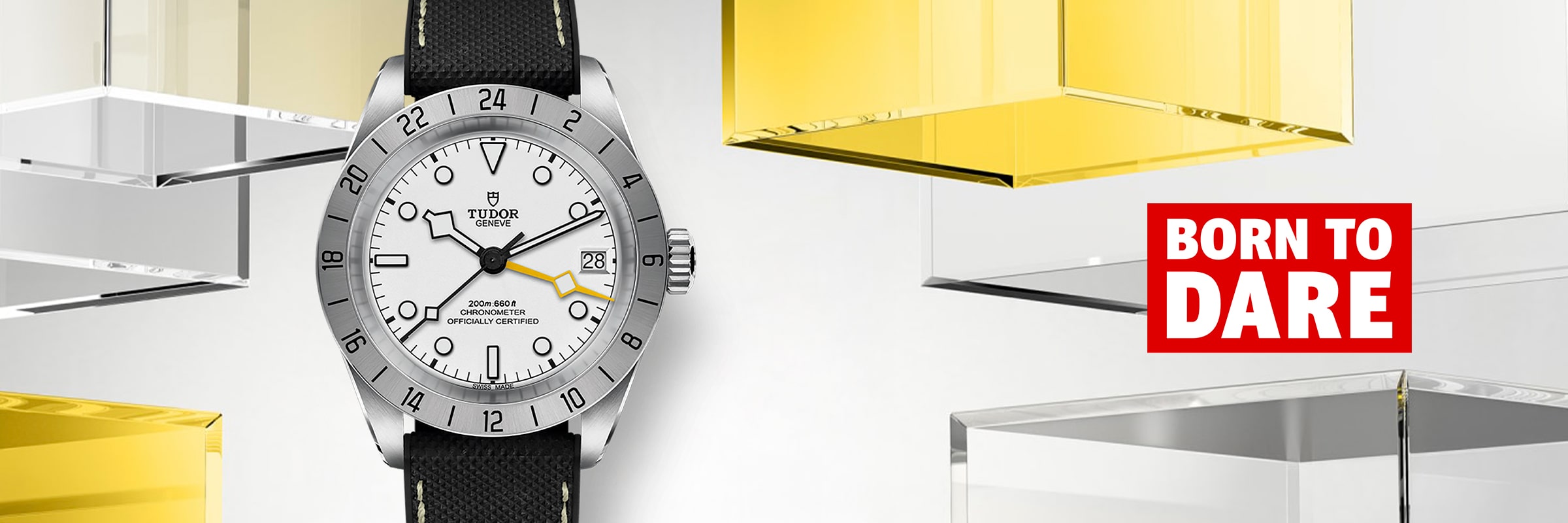 2025 © TUDOR Eine silberne Tudor Black Bay Pro Armbanduhr mit weißem Zifferblatt und schwarzem Armband ist vor einem modernen Hintergrund aus gelben und klaren Würfeln zu sehen. Der Schriftzug "BORN TO DARE" erscheint in fetter weißer und roter Schrift.
