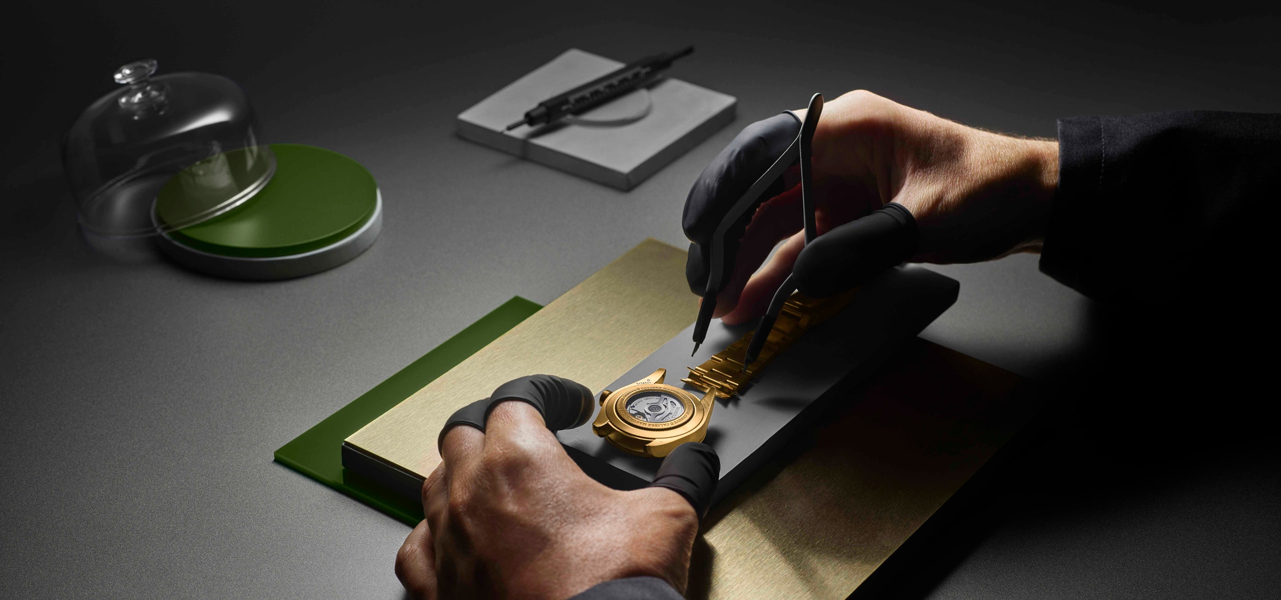 2025 © TUDOR Eine Person mit schwarzen Handschuhen benutzt eine Pinzette, um die Innenteile einer Tudor-Luxusarmbanduhr auf einer Werkbank, umgeben von Präzisionswerkzeugen und -materialien, feinfühlig zusammenzusetzen oder einzustellen.