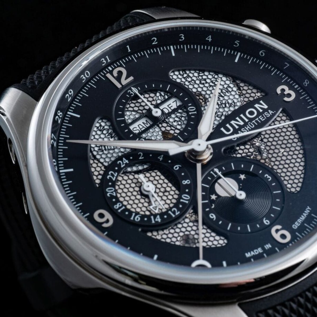 2025 © UNION GLASHÜTTE Nahaufnahme einer luxuriösen Union Glashütte Belisar Armbanduhr mit schwarzem strukturiertem Zifferblatt, silbernen Zeigern und mehreren Hilfszifferblättern, die den Tag, das Datum und die 24-Stunden-Zeit anzeigen, alles in poliertem Edelstahl.