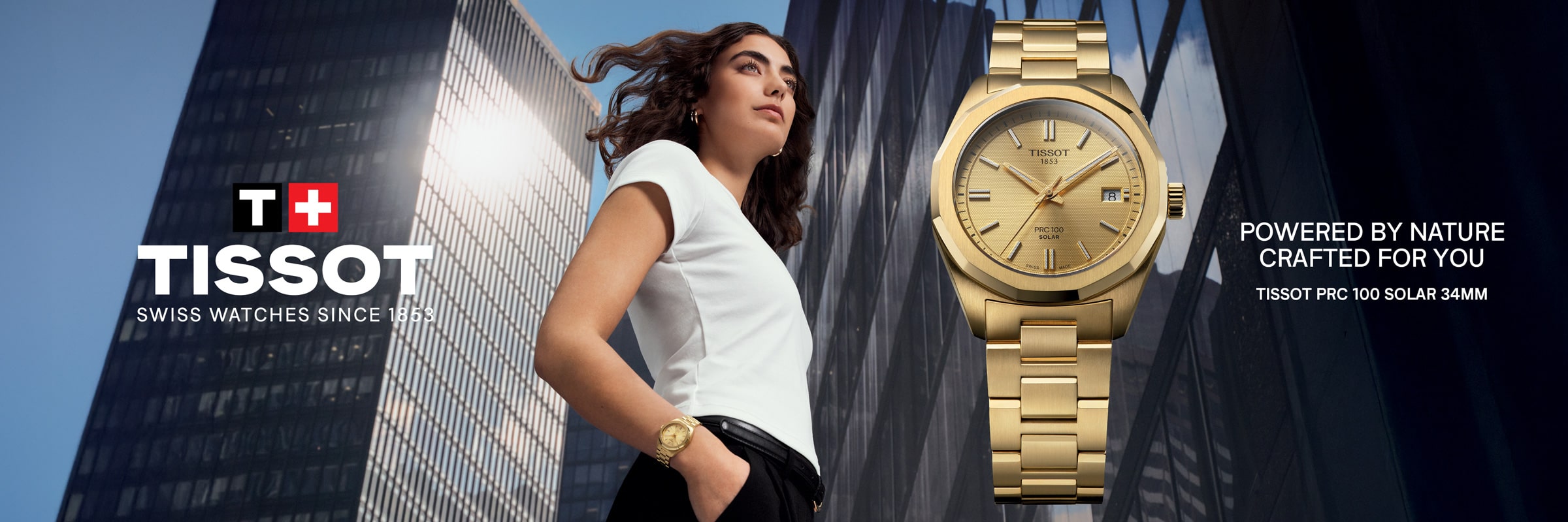 2025 © TISSOT Eine Frau in einem weißen Oberteil und einer goldenen Uhr steht selbstbewusst vor modernen Glasgebäuden. Neben ihr ist eine Nahaufnahme einer goldenen Tissot PRX 100 Solaruhr zu sehen, die das Tissot-Logo und den Slogan trägt.