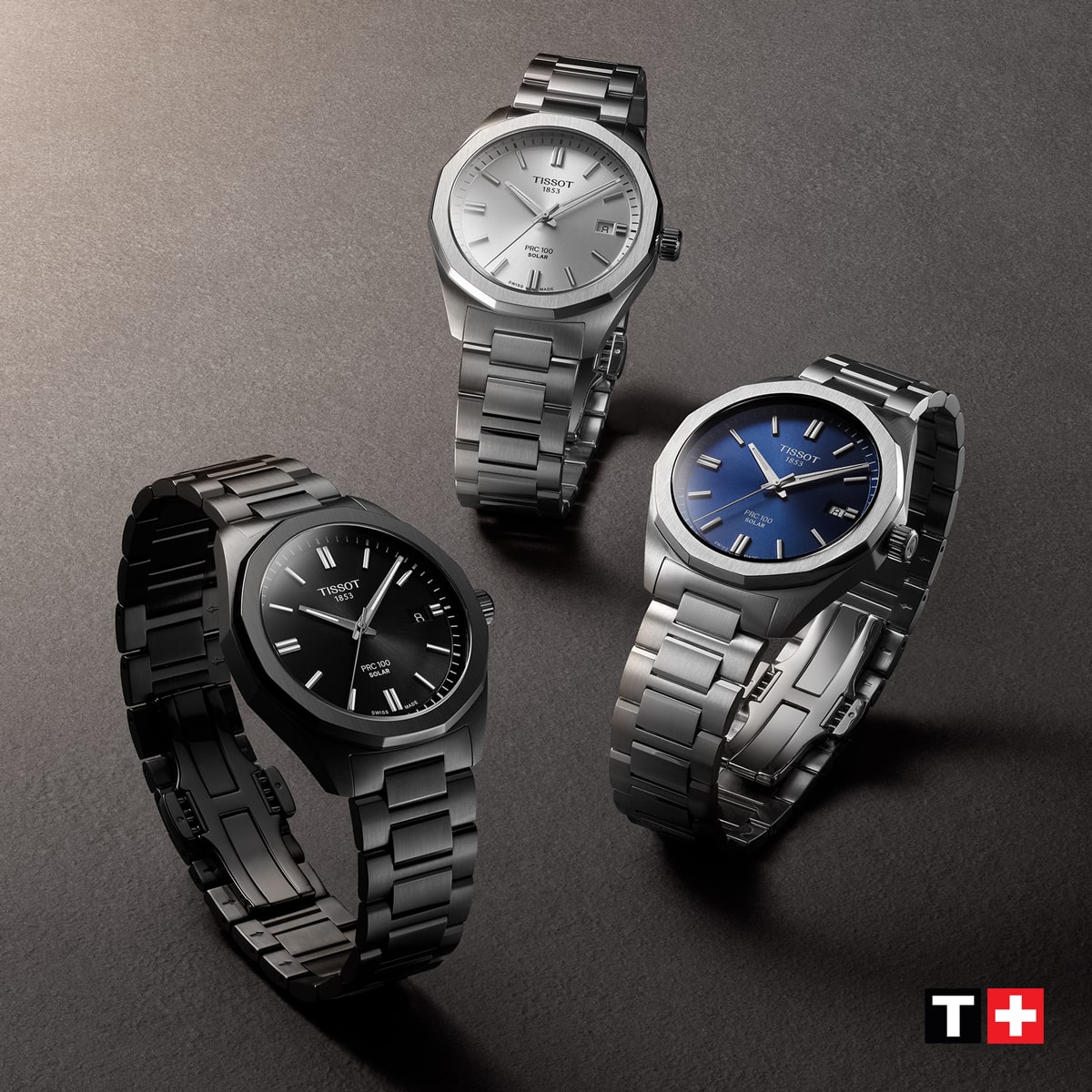 2025 © TISSOT Drei PRC 100 Solar Armbanduhren aus Edelstahl mit Metallbändern sind auf einer grauen Fläche ausgestellt. Die Zifferblätter sind schwarz, silber und blau. Das Tissot-Logo erscheint in der unteren rechten Ecke.