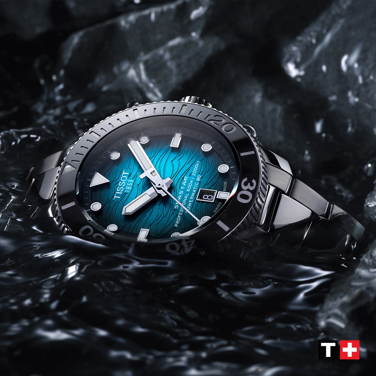 2025 © TISSOT Eine Tissot Seastar-Armbanduhr mit blauem Wellenmuster auf dem Zifferblatt und silbernen Akzenten ruht auf einer nassen, felsigen Oberfläche, die von Wasser umgeben ist. Das Tissot-Logo erscheint in der unteren rechten Ecke.