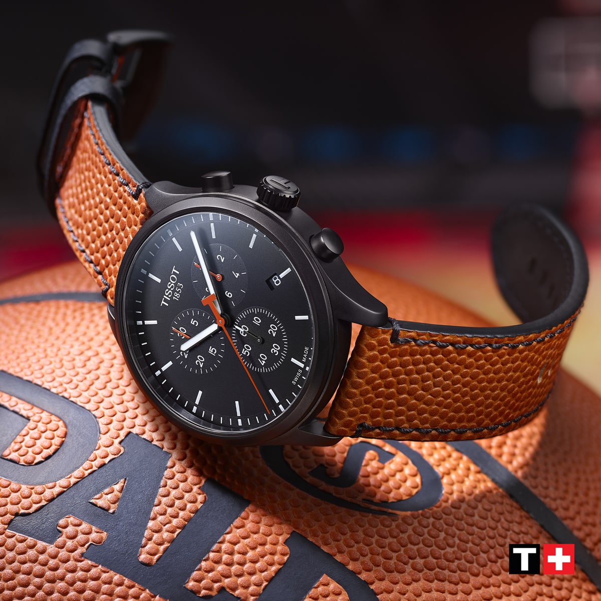 2025 © TISSOT Eine Tissot XL-Chronographen-Armbanduhr mit braunem, strukturiertem Lederarmband ruht auf einem Basketball. Das schwarze Zifferblatt ist mit weißen Markierungen und Ziffernblättern versehen, das Tissot-Logo und das Symbol der Schweizer Flagge befinden sich in der unteren rechten Ecke.