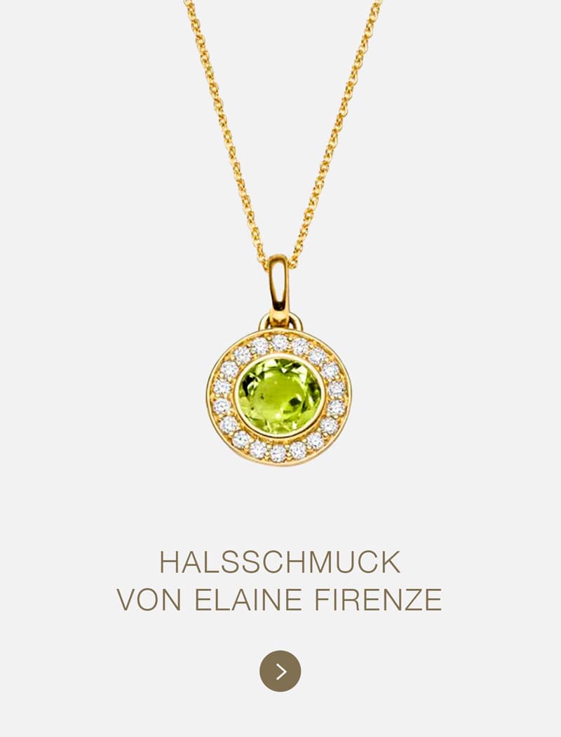 Goldene Halskette mit einem runden grünen Edelsteinanhänger, umgeben von kleinen klaren Steinen, auf weißem Hintergrund. Darunter steht der Text: "HALSSCHMUCK VON ELAINE FIRENZE - entdecken Sie die Eleganz des Schmucks von Elaine Firenze.