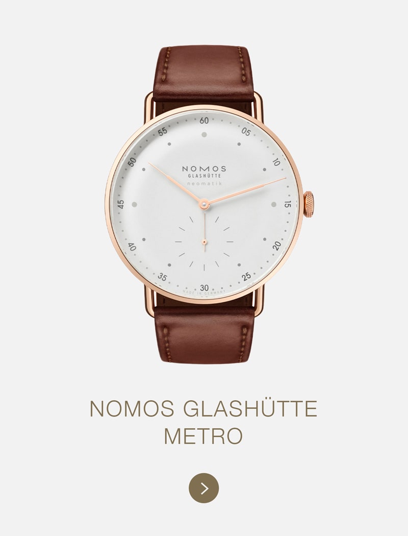 Eine NOMOS Glashütte Metro Armbanduhr mit weißem Zifferblatt, kleiner Sekundenanzeige, roségoldenem Gehäuse und braunem Lederarmband wird auf einem schlichten hellen Hintergrund dargestellt. Unter der Uhr stehen die Marke NOMOS Glashütte und der Modellname.