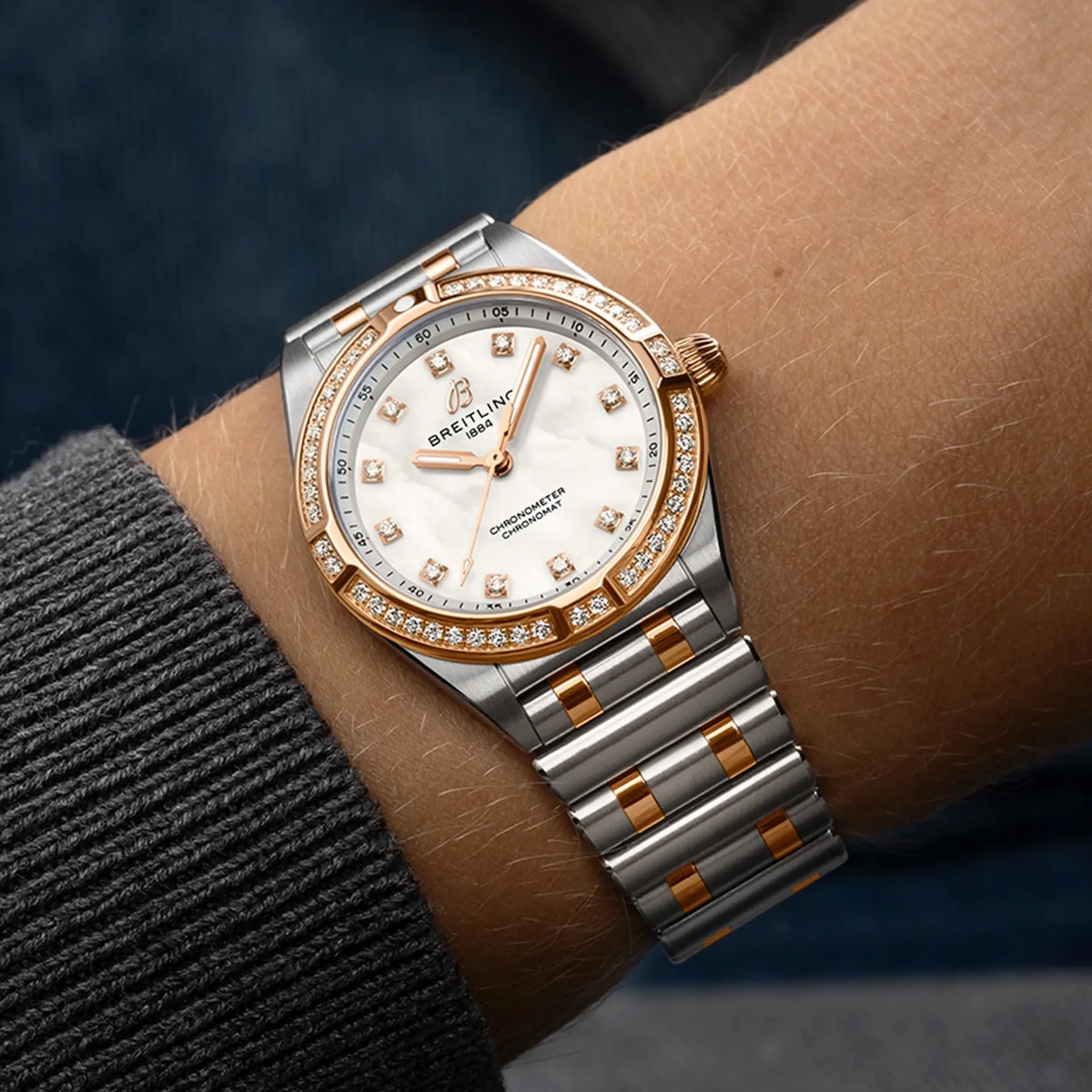 Ein Handgelenk trägt eine luxuriöse Breitling Chronomat Uhr mit einem Armband aus Silber und Roségold, einem Zifferblatt aus weißem Perlmutt, diamantbesetzten Indexen und einer diamantbesetzten Lünette.