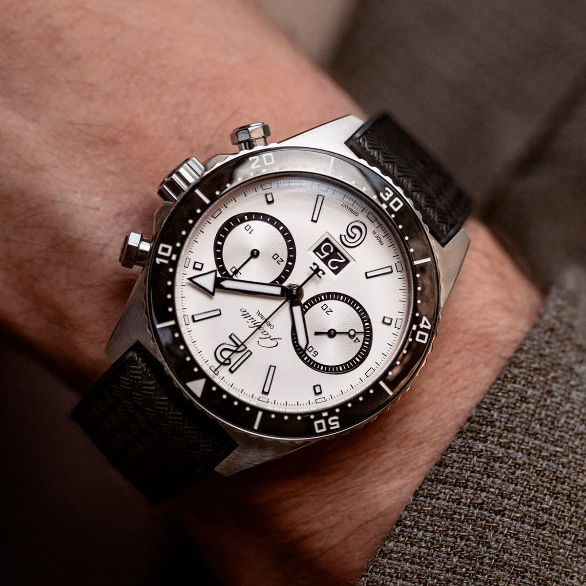 Nahaufnahme eines Handgelenks mit einer Luxus-Chronographenuhr der Spezialist Kollektion mit weißem Zifferblatt, schwarzer Lünette, schwarzem Armband und zwei Hilfszifferblättern, gepaart mit einem braunen Anzugärmel.