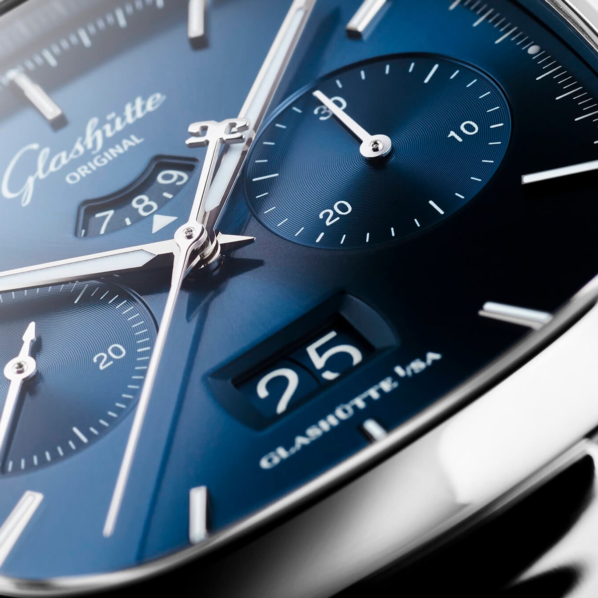 Nahaufnahme einer luxuriösen Glashütte Original Armbanduhr aus der Vintage Kollektion mit blauem Zifferblatt, silbernen Zeigern, Chronographenzifferblättern und einer markanten Datumsanzeige mit der "25" am unteren Rand mit feinen Details und Reflexen.