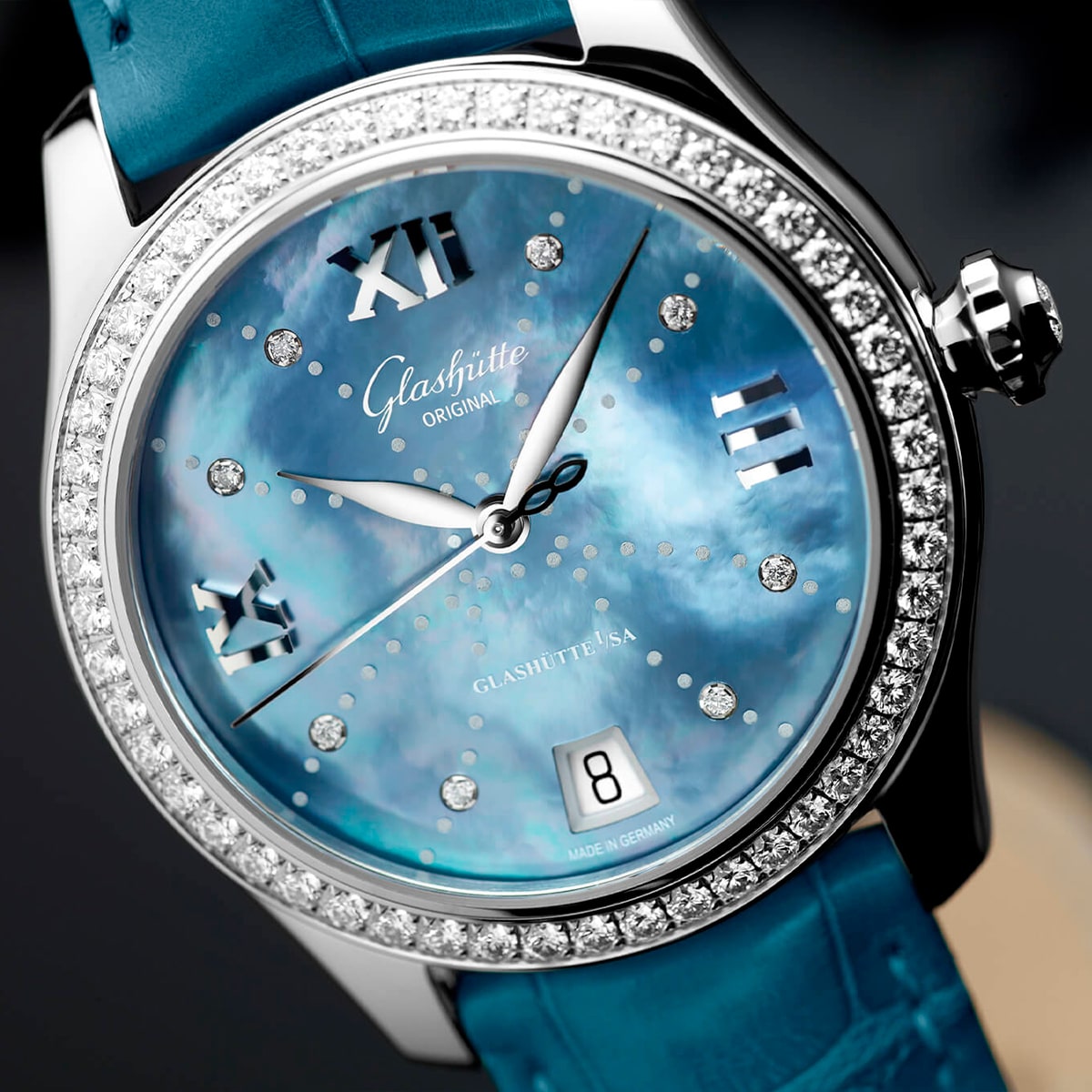 2025 © Glashütte Original Eine luxuriöse Glashütte Original Damenuhr mit blauem Perlmuttzifferblatt, Diamantlünette, silbernen römischen Ziffern und blauem Lederband. Das Datumsfenster ist bei 6 Uhr sichtbar.
