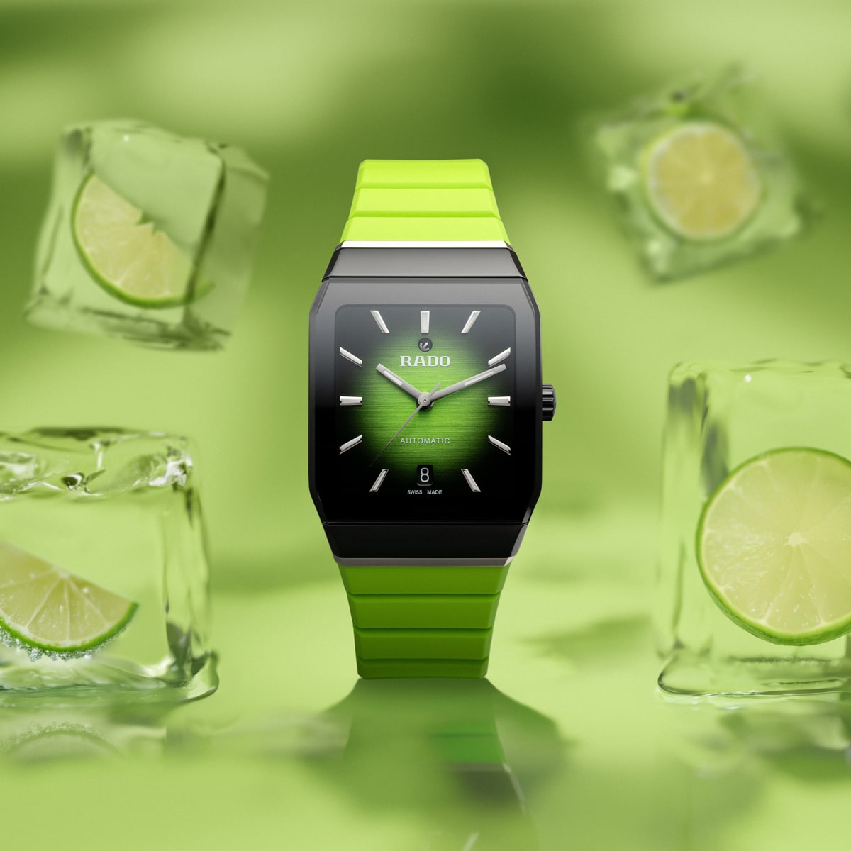 2025 © RADO Eine grüne Rado Anatom-Armbanduhr mit quadratischem Zifferblatt wird vor einem grünen Hintergrund gezeigt, umgeben von schwimmenden Eiswürfeln mit Limettenscheiben im Inneren. Die Uhr hat ein passendes grünes Armband.