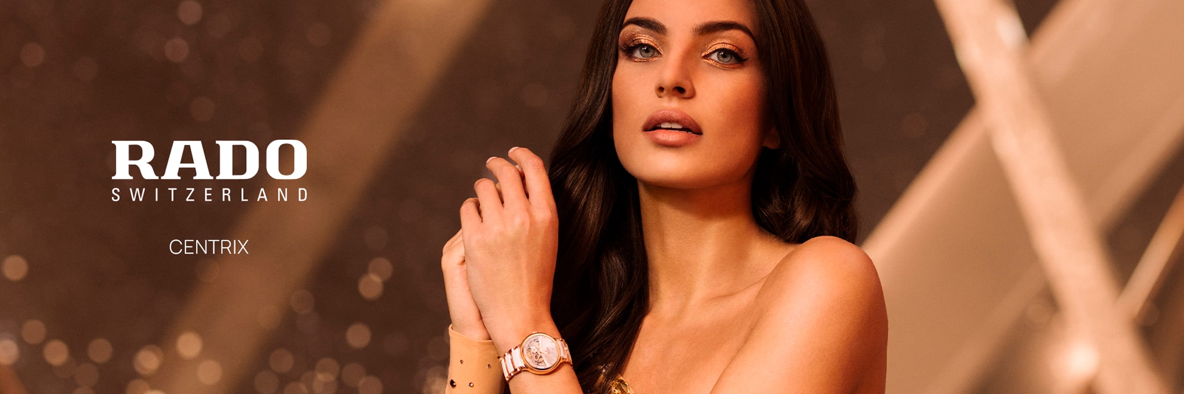 2025 © RADO Eine Frau mit langen dunklen Haaren posiert mit einer goldenen Uhr und eleganter Kleidung. Das Bild hebt den Text "RADO SWITZERLAND CENTRIX" hervor und zeigt die raffinierte Ausstrahlung der Rado Centrix vor einem warmen, sanft beleuchteten Hintergrund in Gold und Braun.