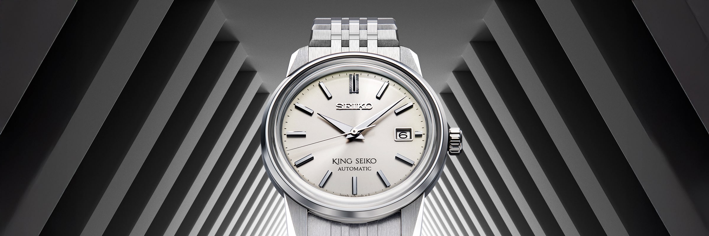 Eine silberne King Seiko-Automatik-Armbanduhr mit weißem Zifferblatt und Datumsanzeige ist mittig vor einem markanten, geometrischen schwarz-weißen Dreieckstunnel-Hintergrund abgebildet.