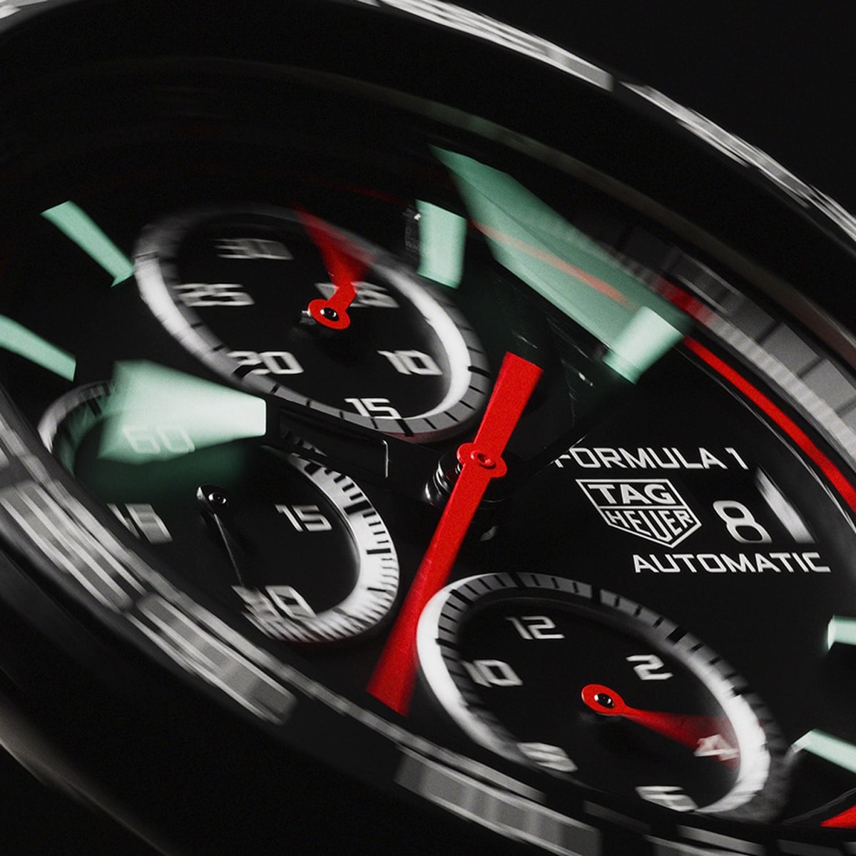 Nahaufnahme des Zifferblatts einer TAG Heuer Formula 1 mit drei Hilfszifferblättern, roten Zeigern und einem Datumsfenster bei 3 Uhr. Das leicht unscharfe Bild fängt die dynamische Bewegung der Zeiger der Formel 1 ein.