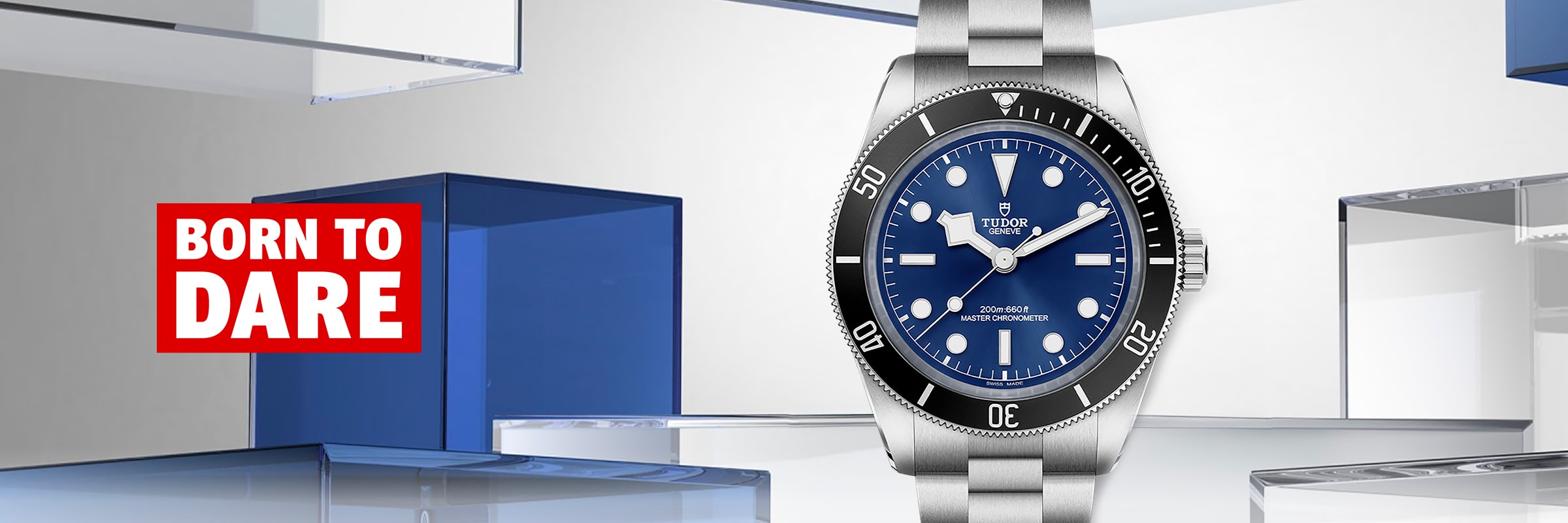 2025 © TUDOR Eine silberne Tudor Black Bay 68 Taucheruhr mit blauem Zifferblatt und schwarzer Lünette wird vor einem modernen Hintergrund aus transparenten blauen und klaren Blöcken präsentiert. Auf der linken Seite steht in fetter roter und weißer Schrift "BORN TO DARE".