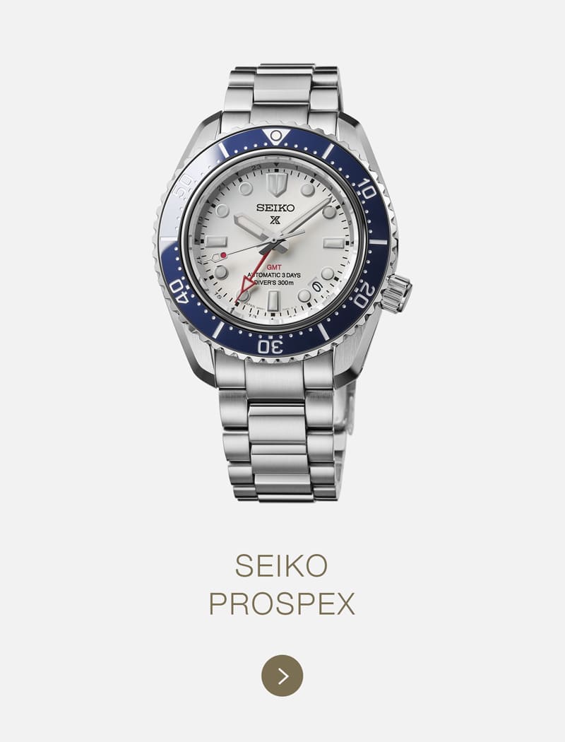 Eine silberne Seiko Prospex-Taucheruhr mit blauer Lünette, weißem Zifferblatt und Metallarmband ist vor einem hellen Hintergrund abgebildet, mit dem ikonischen Seiko-Branding und dem Text "SEIKO PROSPEX" mit einem Vorwärtspfeil darunter.