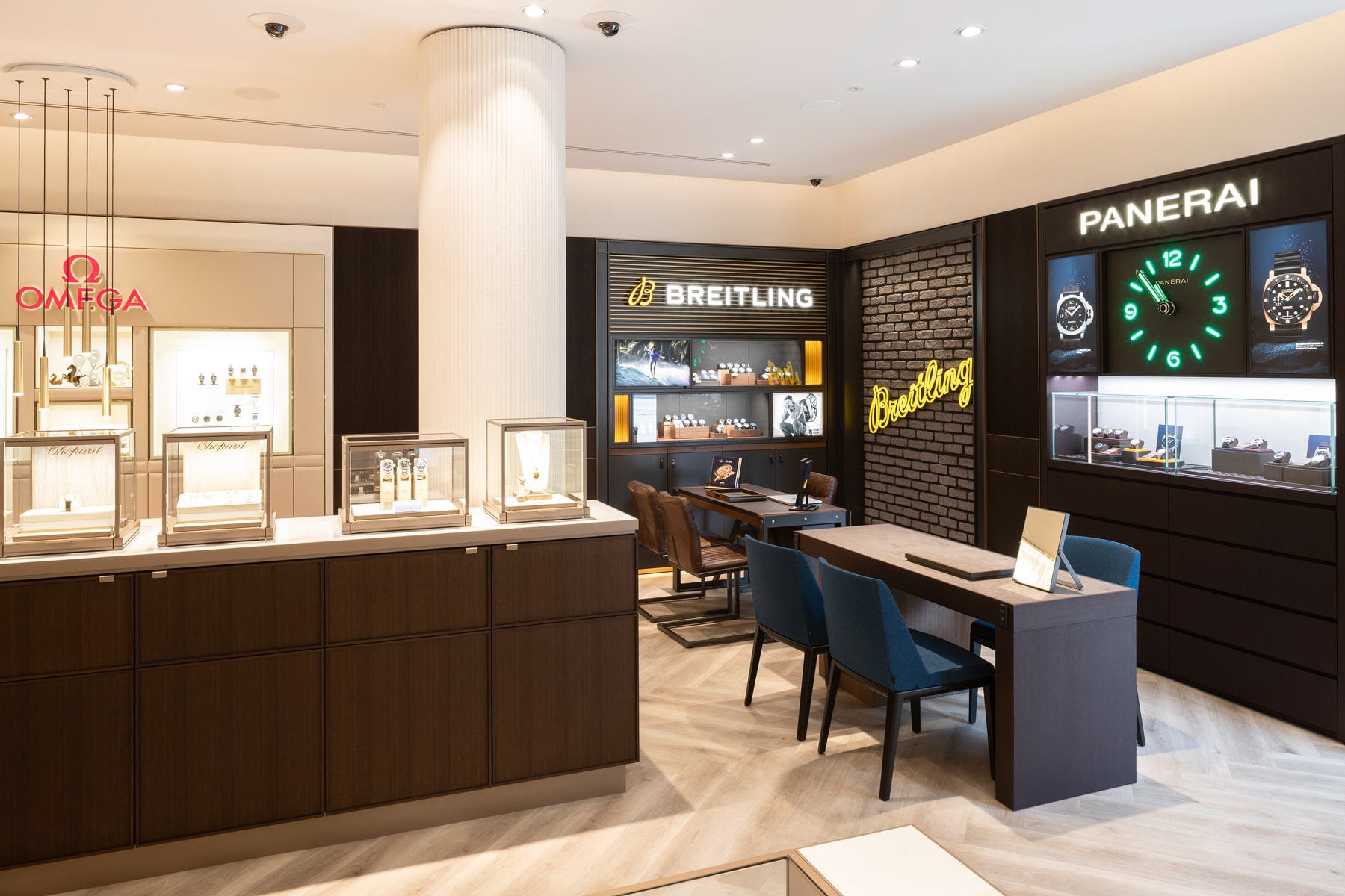 © Juwelier Wenthe Inneneinrichtung eines Luxusuhrengeschäfts mit Auslagen von Omega-, Breitling- und Panerai-Uhren. Elegante Holz- und Glasvitrinen, blaue Stühle und beleuchtete Markenschilder schaffen eine moderne, gehobene Einkaufsatmosphäre.