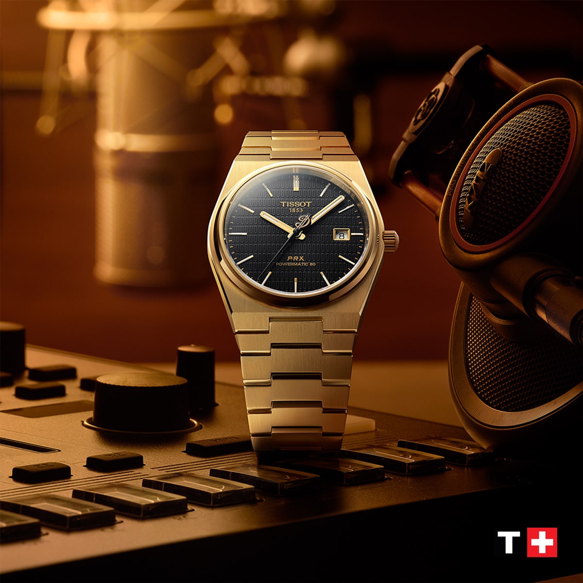 Eine silberne Tissot-Armbanduhr mit dunklem Zifferblatt ist auf einem Musikmischpult neben einem Kopfhörer zu sehen. Die Szene ist warm beleuchtet, und das Tissot-Logo ist in der unteren rechten Ecke zu sehen.